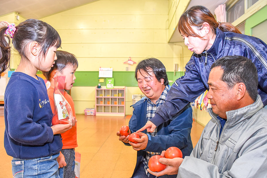 トマト生産者が子供にトマトを手渡している様子の写真