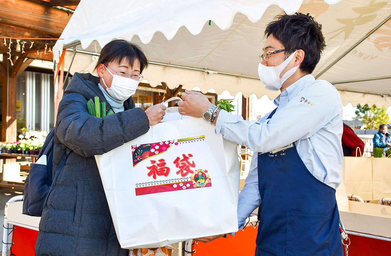 野菜の福袋を手渡す夢未市の清田店長（右）の写真