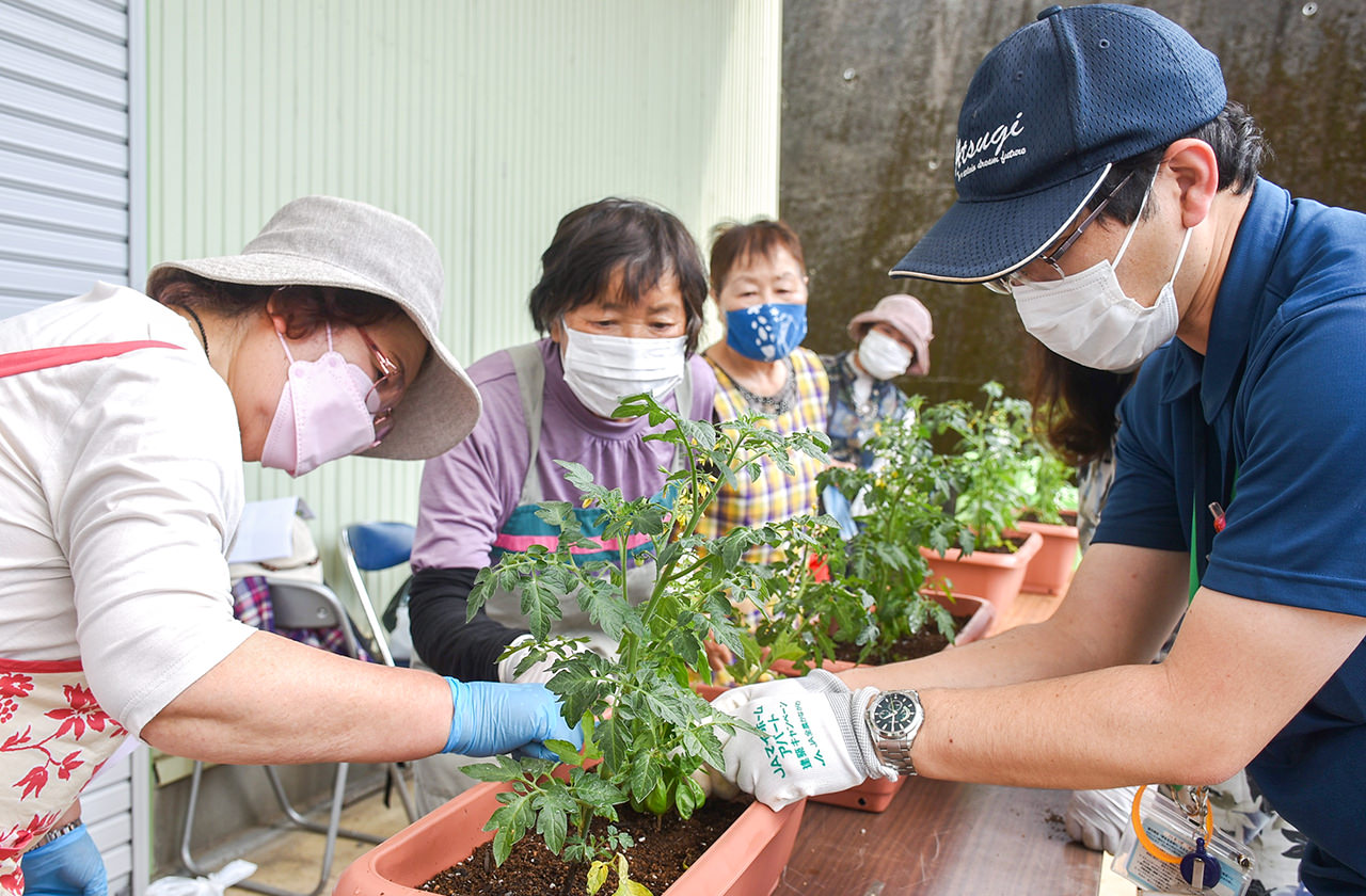 営農指導員（右）から苗の定植方法を学ぶ部員らの写真