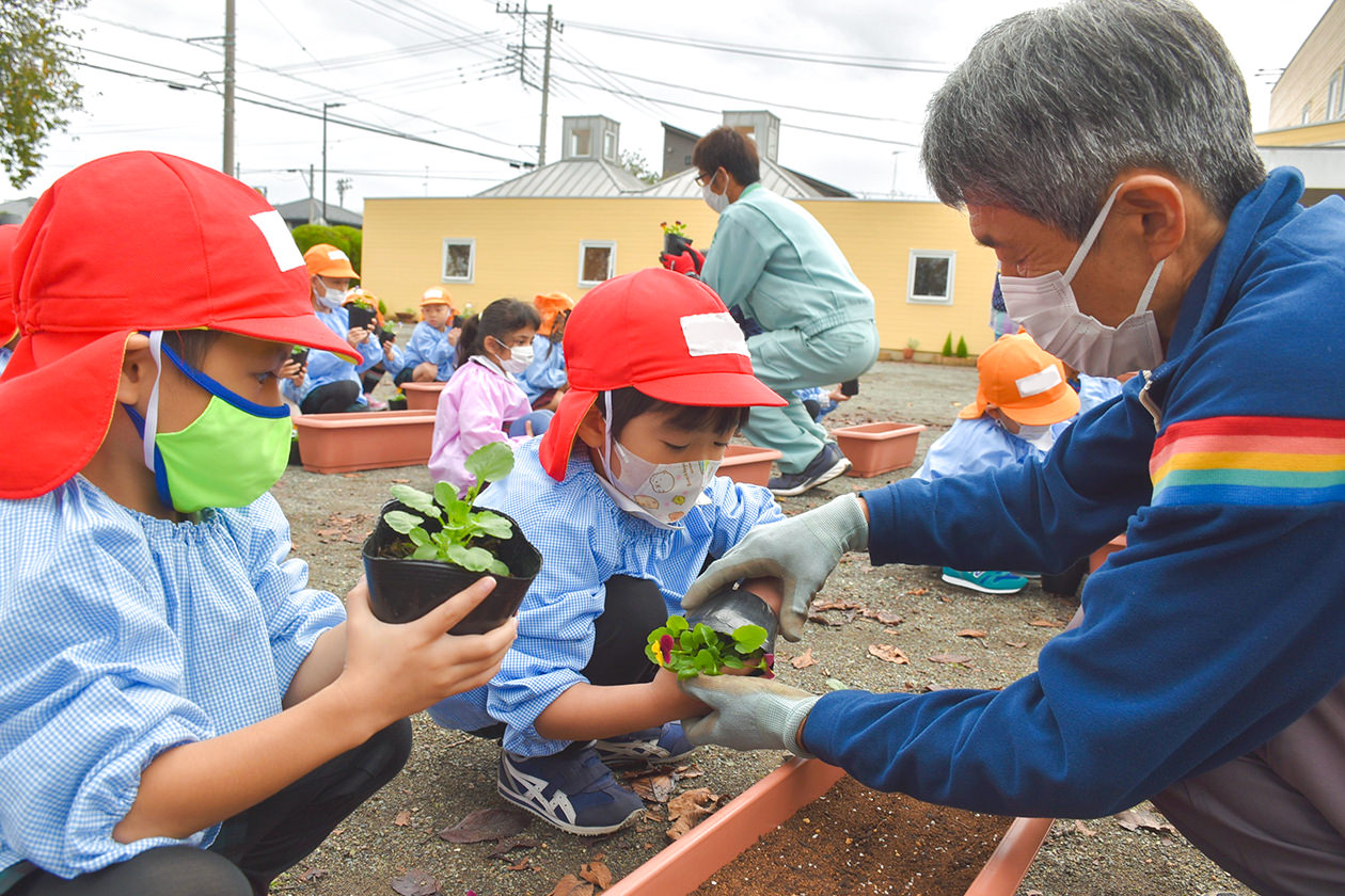 委員と共に植え付けを行う園児らの写真