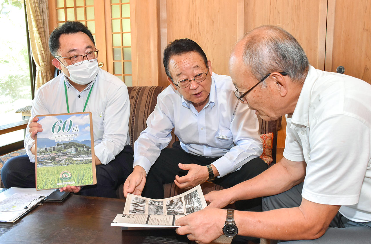 60周年記念誌で歴史を振り返る大貫組合長（中）と総代（右）の写真